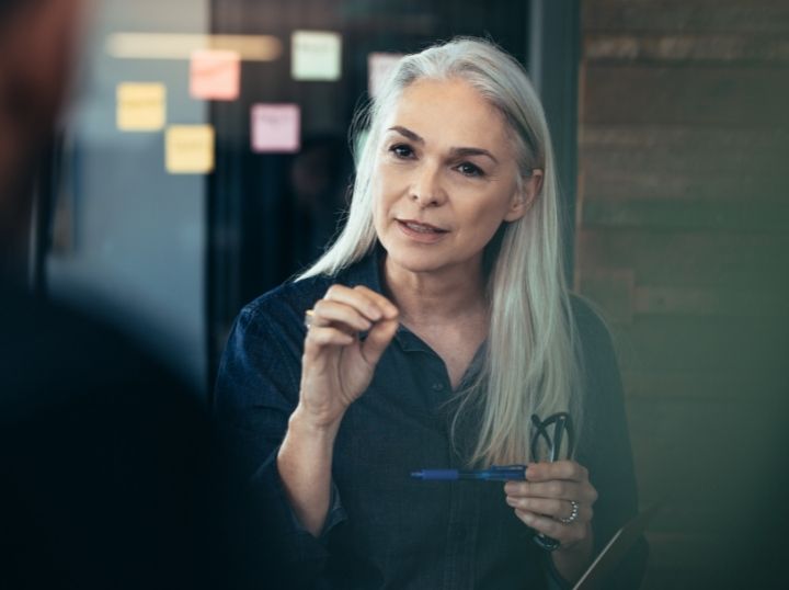 lady in the picture holding a pen and glasses having a conversation