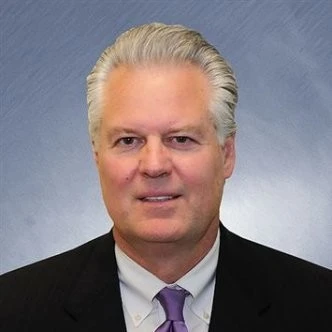 Portrait of a confident professional man with white hair, wearing a dark suit, white shirt, and purple tie
